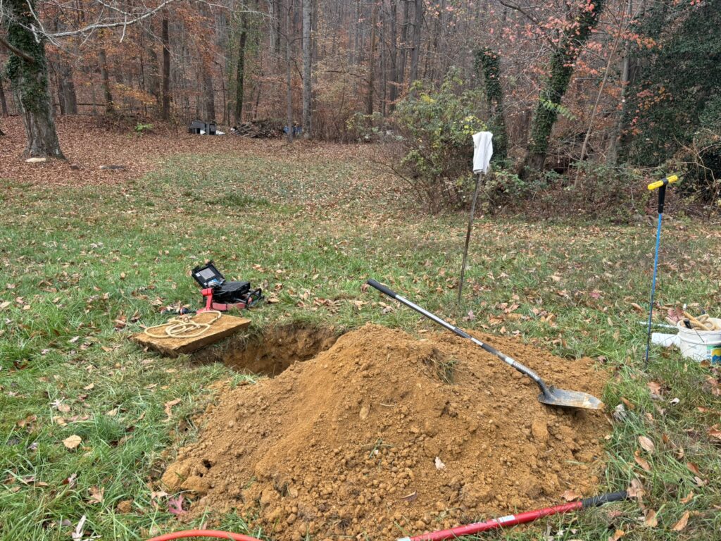 A site of a septic inspection, with the septic tank cover dug out, and a sewer scope in the background. Additional services like these affect the overall home inspection cost.